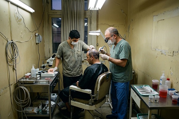 A pseudo-specialist performs a black market hair transplant under precarious health conditions