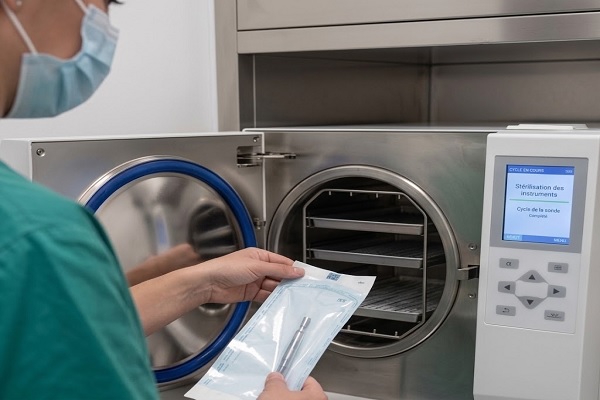 Gros plan sur une technicienne masquée stérilisant des instruments dans un autoclave moderne, soulignant les exigences légales pour les cliniques capillaires agréées en Espagne
